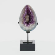 Poliertes Amethyst-Ei aus Uruguay auf Metallständer mit sichtbarer Achatstruktur außen und funkelnder Amethyst-Druse im Inneren.