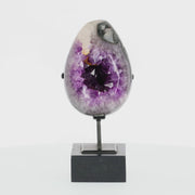 Poliertes Amethyst-Ei aus Uruguay auf Metallständer mit sichtbarer Achatstruktur außen und funkelnder Amethyst-Druse im Inneren.
